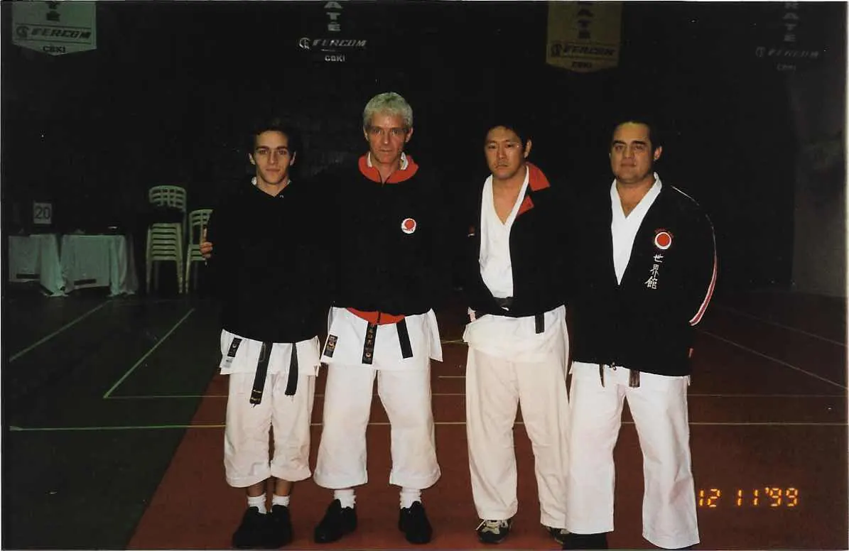 Quatro karatecas de quimono preto em ginásio, foto com data impressa de 12 de novembro de 1999